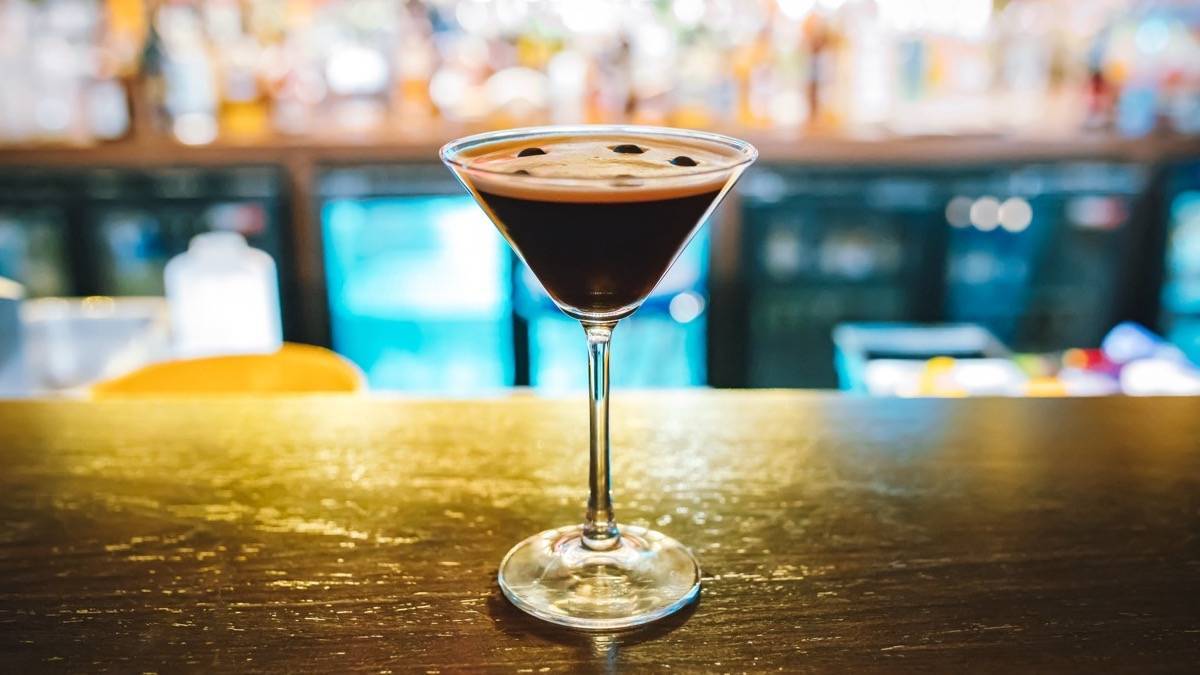 Dark martini on a bar with blurred lights and bottles in the background